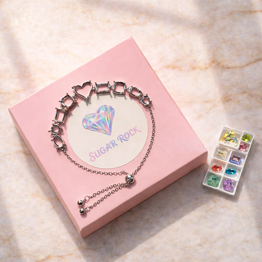 Bracelet with heart-shaped charm on a pink box with 'SUGAR ROCK' text, on a light marble background.